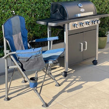 Blue camping chair and black outdoor gas barbecue grill on patio with greenery background