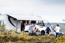 Modern motorhome with awning, family relaxing and playing outdoors in scenic nature