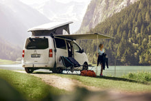 Campervan with Thule 3200 awning extended by lake, mountain scenery, camping gear visible