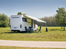 Motorhome with extended awning, outdoor chairs and table on grassy field, sunny weather
