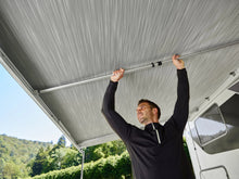 Man installing an aluminium tension rafter on a campervan awning outdoors