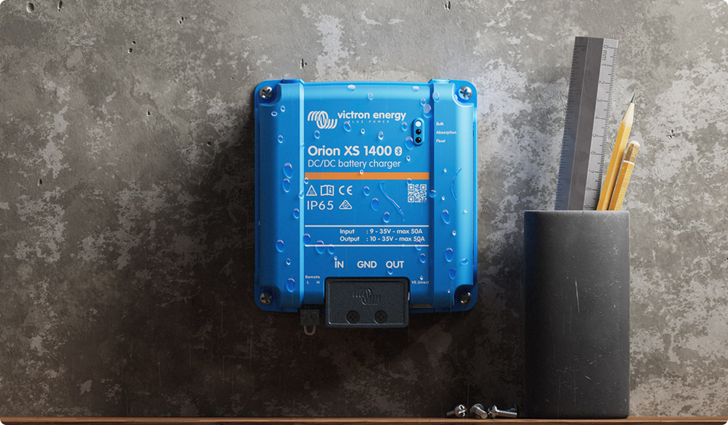 A blue Victron Energy Orion XS 1400 0 XC-DC battery charger mounted on a textured gray wall, with a pencil holder and ruler nearby.